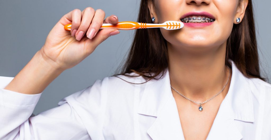 smiling woman medic with braces with great teeth holding tooth brush isolated white wall scaled