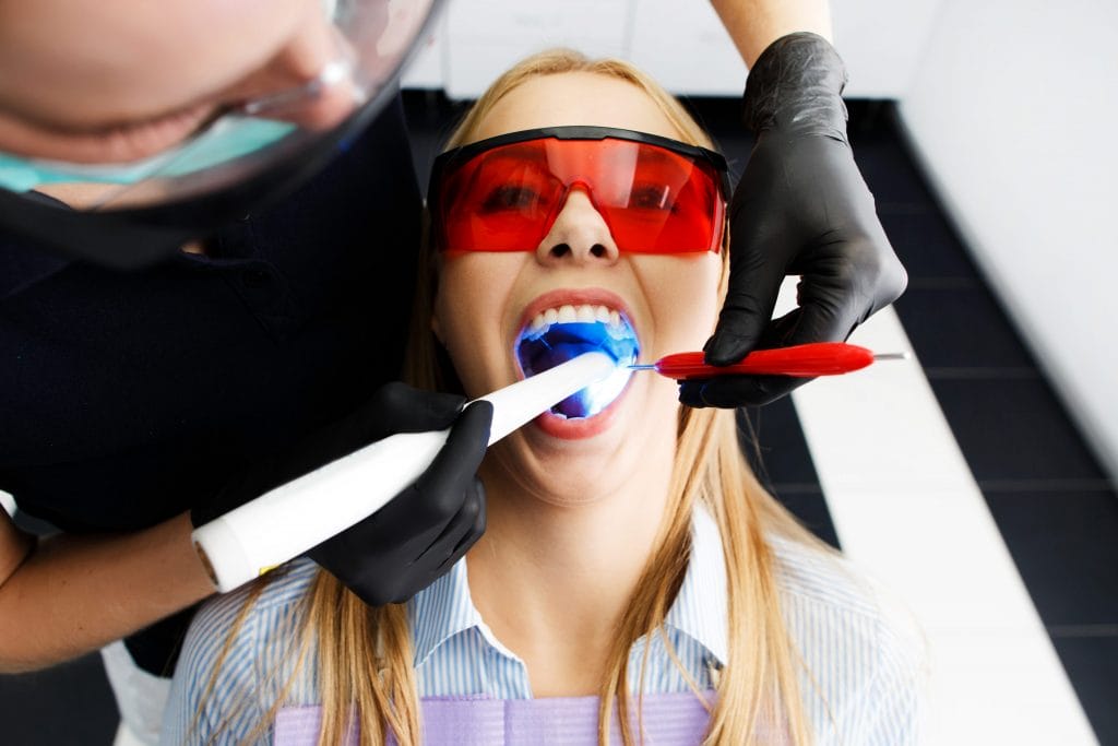 patient red glasses sits chair dentist office while doctor whiten her teeth
