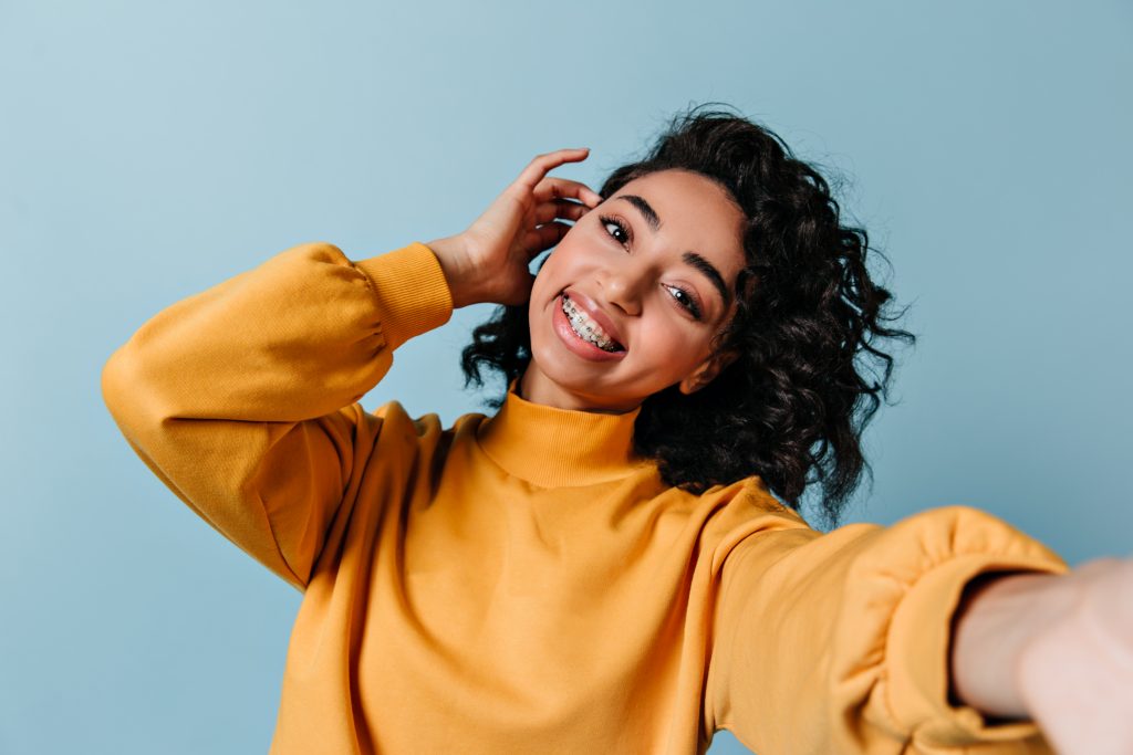 Pleased girl in dental braces taking selfie. Studio shot of gorgeous woman in yellow sweatshirt