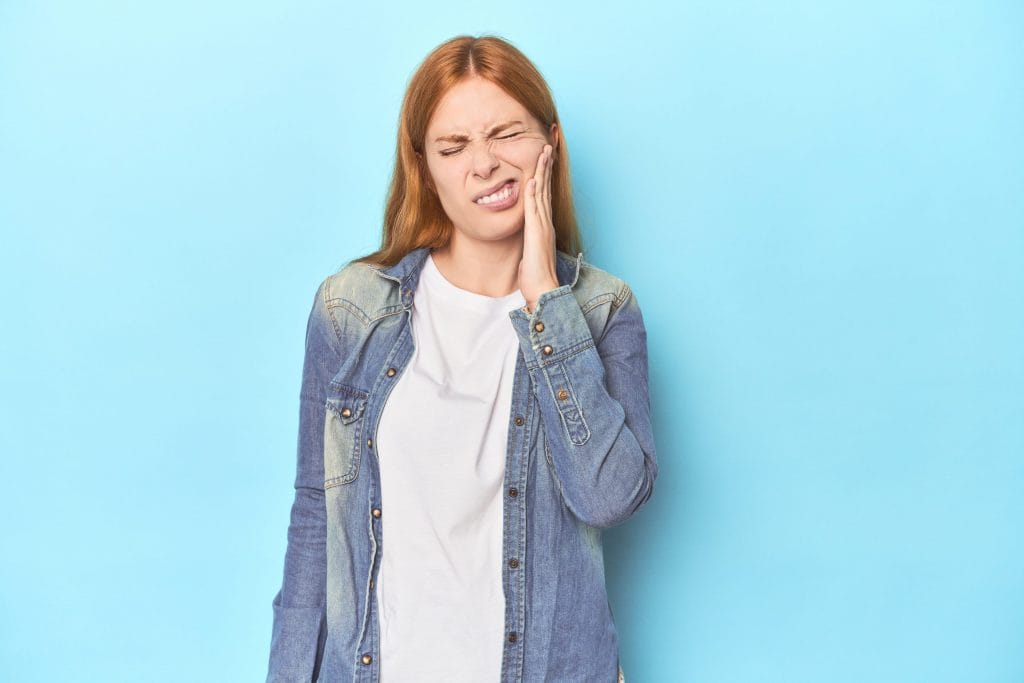 redhead young woman blue background having strong teeth pain molar ache