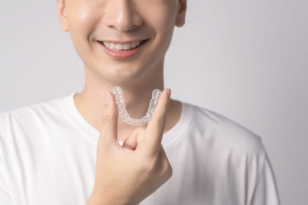 young smiling man holding invisalign braces white background studio
